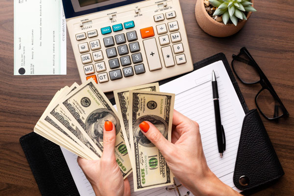Woman's hands holding money and pen on desk, signing a contract.